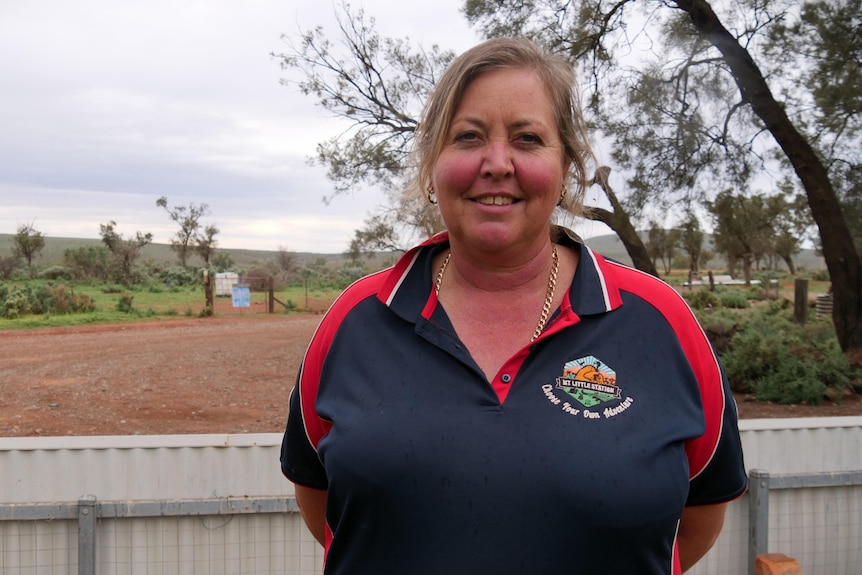 A woman stands in front of a vast outback.