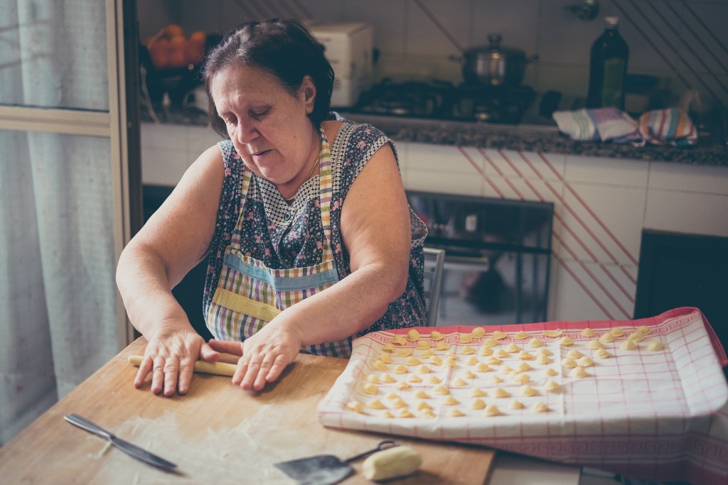Italian woman making homemade gnocchi on a wooden board.
