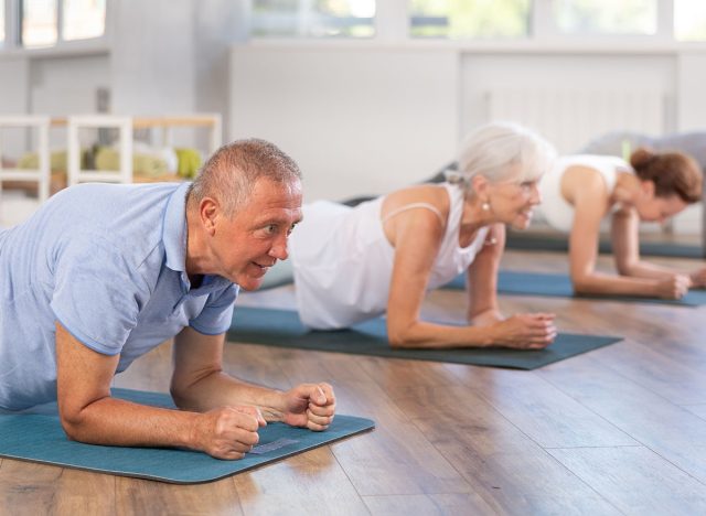 Active pensioners in sportswear doing plank exercise during group pilates training in fitness studio