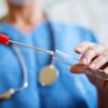 A person in a blue medical scrub holds a test tube and a cotton swab.