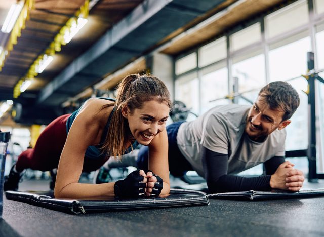 Happy sports couple doing plank exercise while exercising in the gym. Copy space.